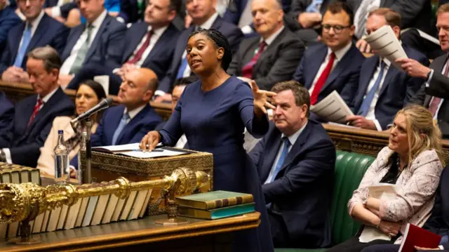 kemi badenoch, dressed in a navy blue suit dress, gestures with her hands at the dispatch box in the House of Commons