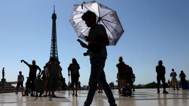 A tourist holding an umbrella to protect himself from the sun as he walks at Trocadero square next to the Eiffel Tower