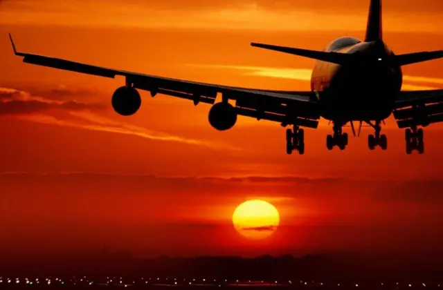 A plane is seen landing against a sunset, the sky is orange and red.
