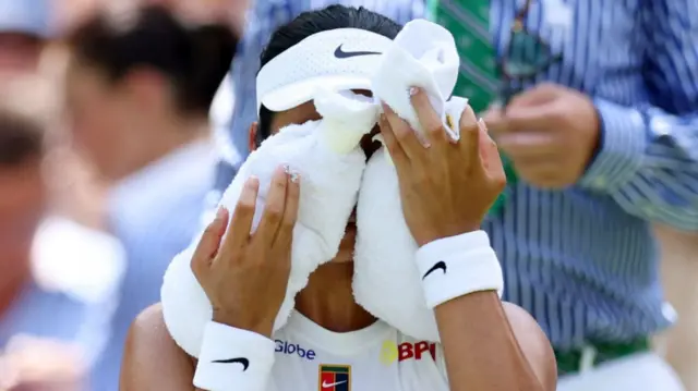 A tennis player covers her face with two cold white towels during a match