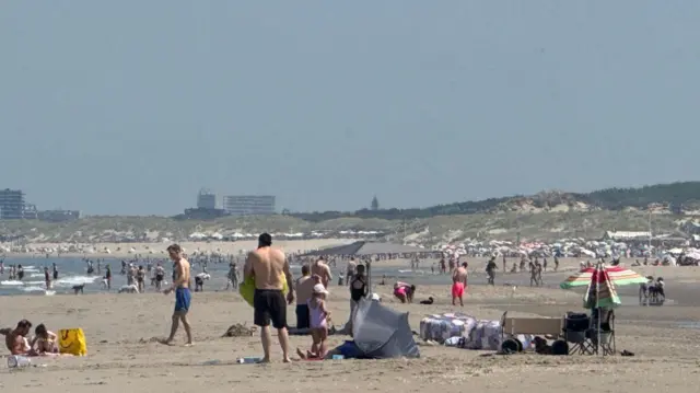 A busy beach in The Hague, the Netherlands, people standing on sand and entering the water.