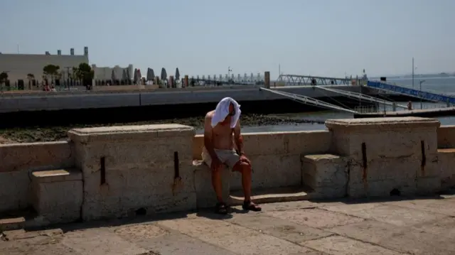 A man covers his head with a t-shirt to hide from the sun as temperatures rise in Lisbon, Portugal, June 30, 2025.