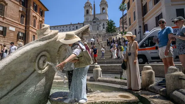 A woman wets her hair at a boat-shaped fountain in front of the Spanish Steps in Central Rome, people queuing behind her to also use the water