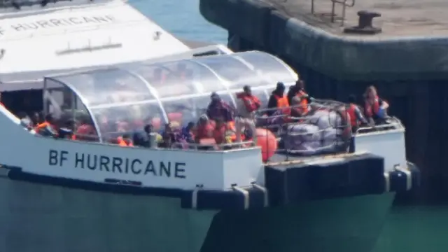 A boat with the words BF Hurricane on the front. Lots of people sit packed together on it