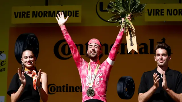 Ben Healy with his arms aloft on the podium after winning stage six of the 2025 Tour de France