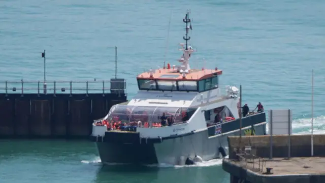 A large boat full of people pulling into a harbour