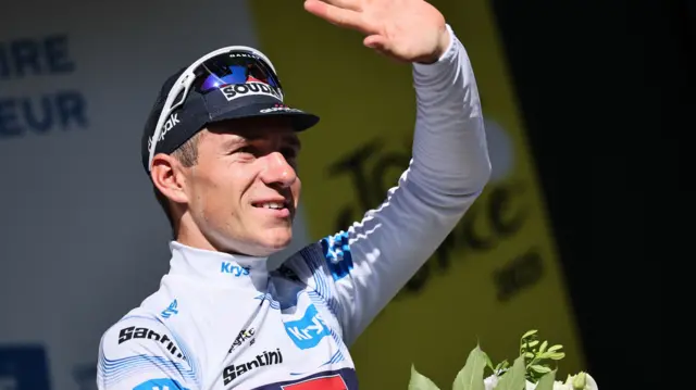 Remco Evenepoel waves on the podium after stage six of the 2025 Tour de France