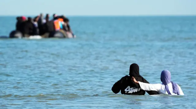 People thought to be migrants wade through the sea to board a small boat leaving the beach at Gravelines, France, on 17 June