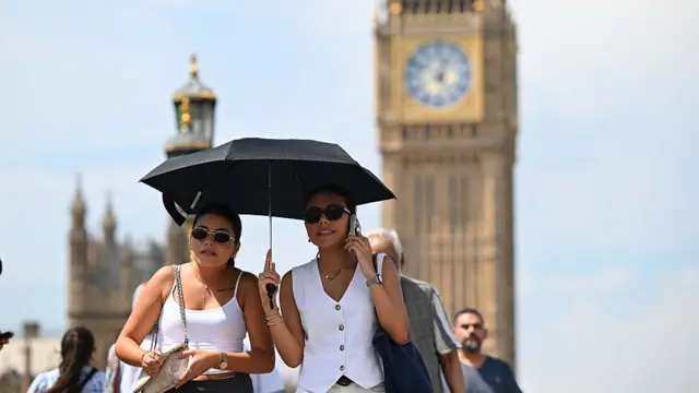 Two women walk in front of Big Ben, holding an umbrella and wearing sunglasses.
