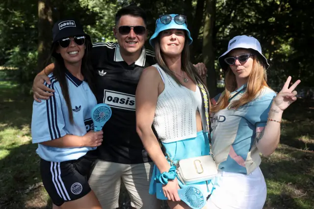 Three women wearing bucket hats, T-shirts and shorts and a man in an Oasis T-shirt and shorts pose for the camera