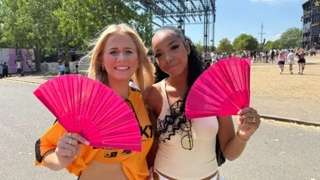 Two young women hold up fans at a music festival.