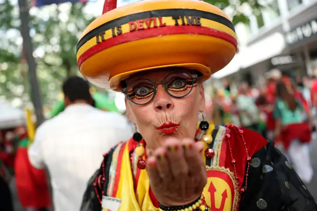Belgium fan with a cheese wheel hat blows a kiss at the camera