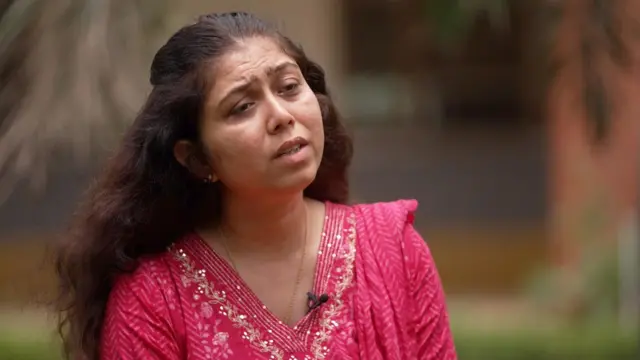 Shweta Parihar speaks to a BBC reporter who is out of shot in an outdoor area that's blurred. She has long dark hair and is wearing a pink top.
