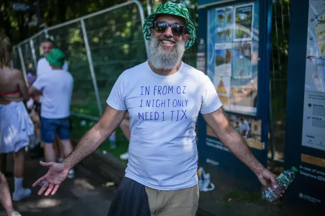 A bearded man in a green bucket hat wears a white T-shirt, which reads: In from Oz 1 night only need 1 tix