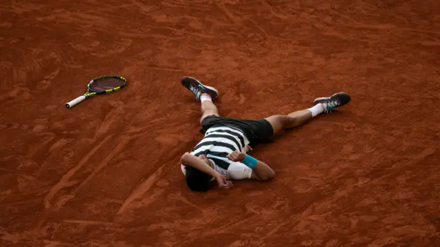 Carlos Alcaraz lies on the clay at the French Open