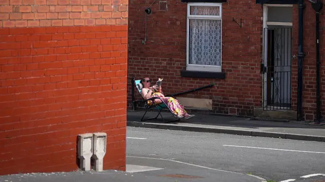 A woman relaxes on a lounge chair outside a home reading a book on an empty street in Leeds.