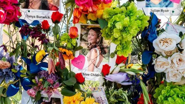 Photos and names of the victims are hung along a wall of flowers