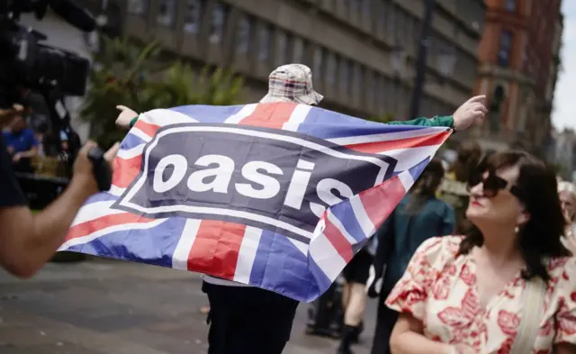 An Oasis fan holds a Union Jack flag featuring the band logo in Cardiff, ahead of the first show in the band's long-awaited reunion tour,
