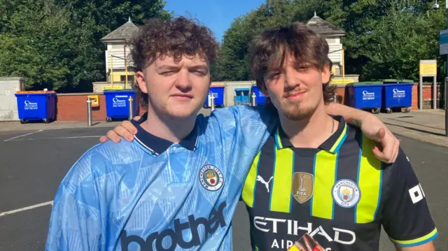 Sean O’Neill, 19, and Paul Maguire, 20, are both wearing Manchester City football shirts. They have their arms around each others' shoulders and are smiling at the camera.