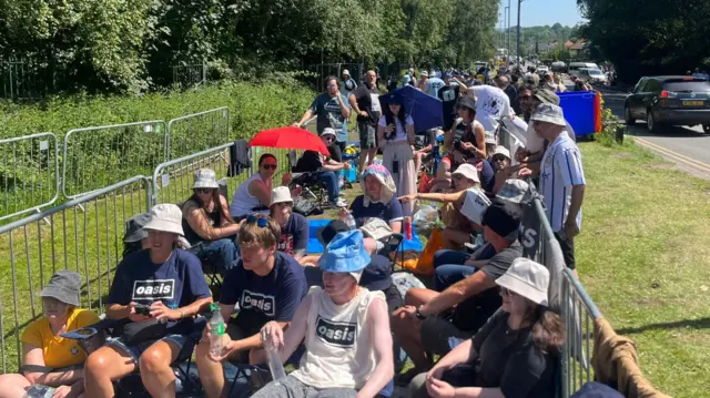 A queue of people are waiting in the glorious sunshine at Heaton Park