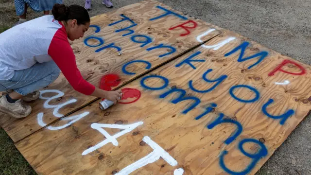 A woman spray paints a sign that reads "Trump, Thank you for coming" with a heart