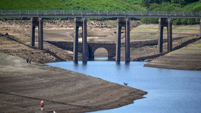 People walk on the dried up bed of Baitings Reservoir as the water level continues to drop on the eve of a hosepipe ban on July 10.