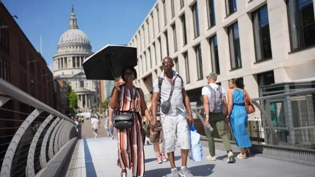 A couple walk hand in hand, with the woman holding an umbrella to shield from the sun