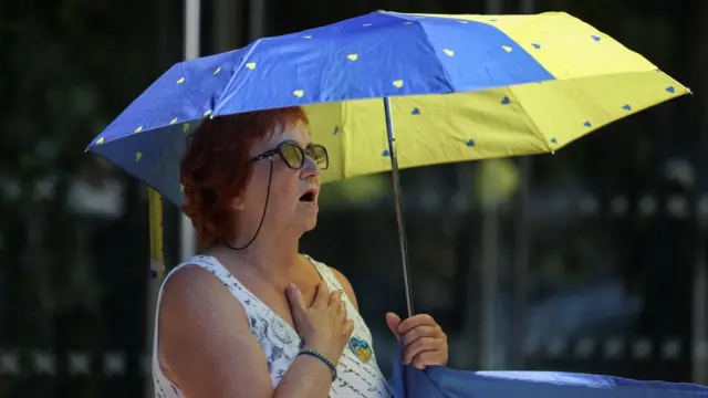 A woman uses an blue and yellow umbrella to cover herself rom the sun