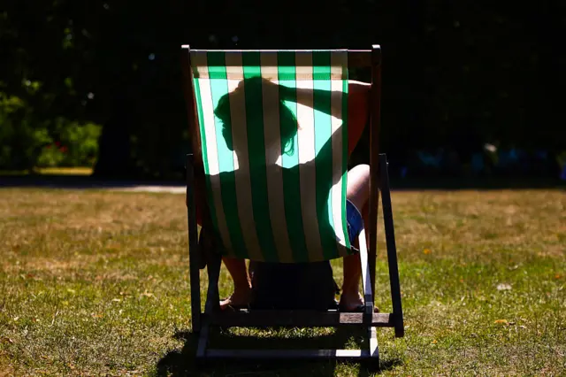 A person sleeps in a green and white striped deckchair in St James's Park on a sunny day.