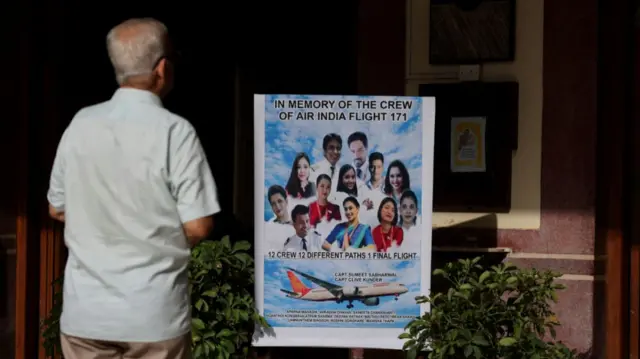 A man faces a poster that has the pictures of all 12 crew who died on the Air India flight