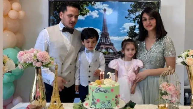 A man stands with his wife and two children as they cut a birthday cake