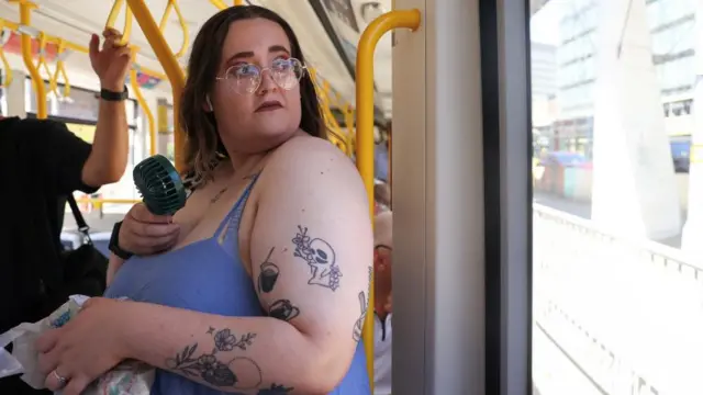 A woman holds a personal fan while riding on the Manchester Metrolin