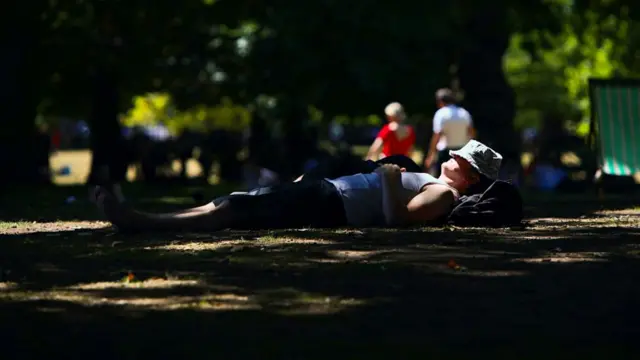 A person sleeps in a park with a hat covered over their eyes during the UK's heatwave.