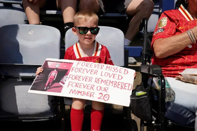 A young Liverpool fan holding a banner in tribute of Liverpool player Diogo Jota ahead of the pre-season friendly match at Deepdale Stadium, Preston.