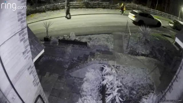Doorbell camera footage of a front porch and street, with Gordon and Marten in the distance walking in the road