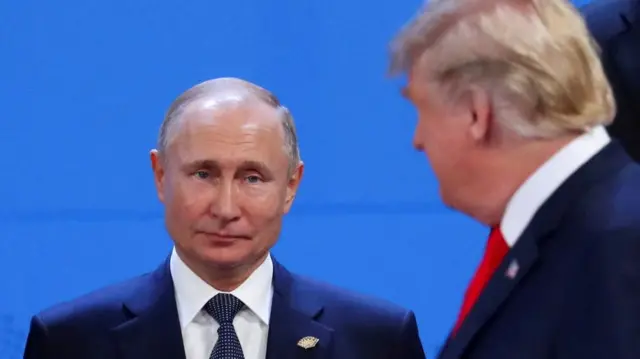putin looks at the camera. trump has his head turned towards putin but you can't see his face. both men are in suits.