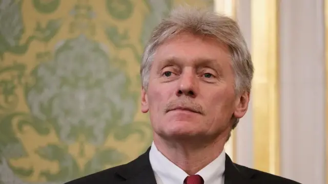 Dmitry Peskov stood in front of a wall decorated in yellow and green