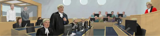 A wide view of the court room with the two defendants in the dock on the left, two rows of barristers and computer screens, the jury against the far wall and the judge in her red robes on a raised bench on the right