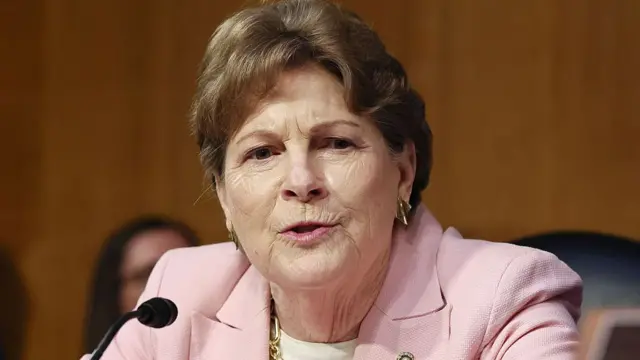Jeanne Shaheen wears a pink blazer and sits in front of a microphone