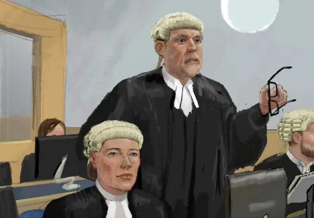 Prosecutor Richard Wright KC stands in a black robe and cream wig gesticulating with his glasses. Rebecca Brown is sitting next to him wearing a black gown and cream wig