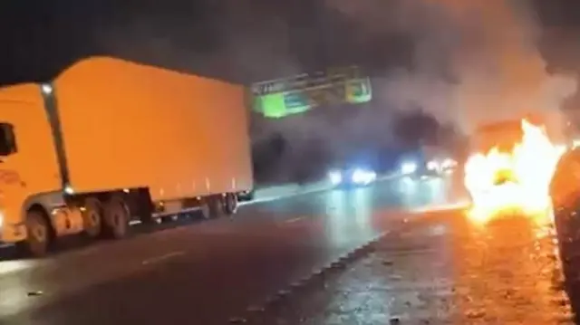 A car on fire by the side of the road