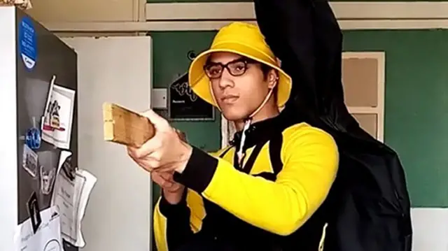 Nicholas Propser wearing a yellow and black uniform and holding a piece of wood as if it was a firearm