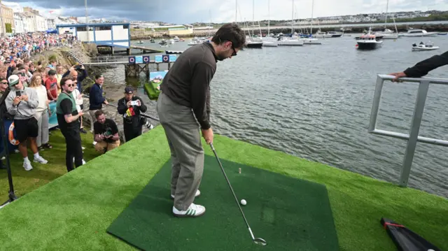 Niall Horan hitting a golf shot at Portrush harbour