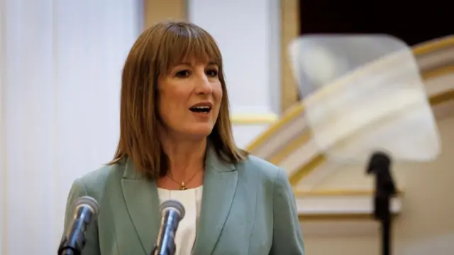 Reeves speaks at Mansion House behind microphones, wearing a blazer and white top.