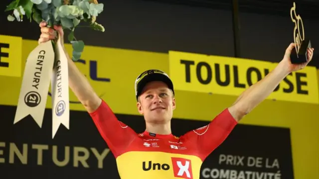 Jonas Abrahamsen with his arms aloft on the podium after winning stage 11 of the 2025 Tour de France