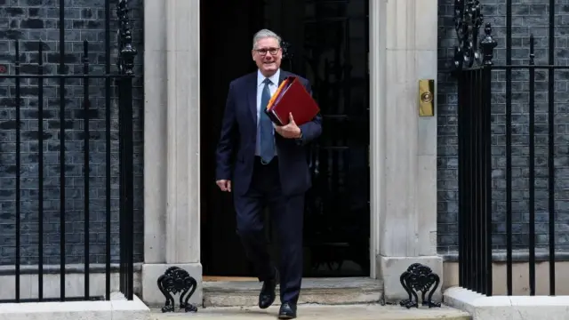 Starmer smiling as he makes his way out of Number 10 holding a red folder