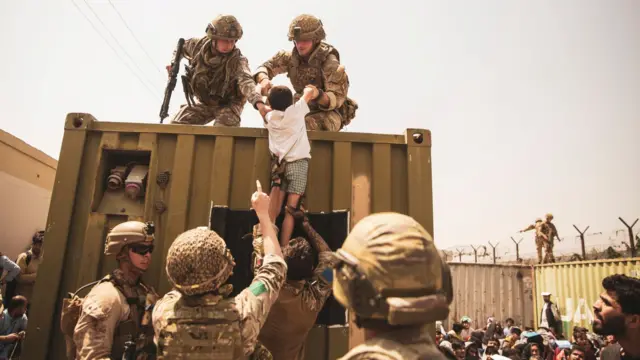 Soldiers on the ground lift up a child to soldiers raised on a mental container as an evacuation at Hamid Karzai International Airport, Kabul, Afghanistan, takes place (file photo from August 2021)