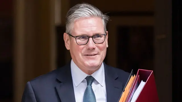 Starmer smiles wearing suit leaving Downing St.