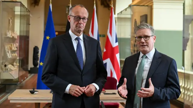 Merz and Starmer stand beside each other, wearing suits and glasses.