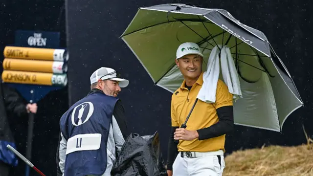 Li Haotong smiles under an umbrella after finishing his round at Royal Portrush